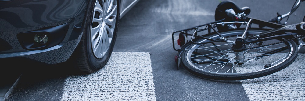A bicycle lies on its side next to a car at a pedestrian crosswalk, suggesting a possible hit-and-run bicycle accident.