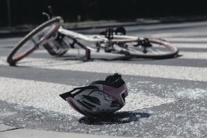 A bicycle lies on its side on a crosswalk next to a helmet and scattered broken glass, suggesting a recent hit-and-run bicycle accident.