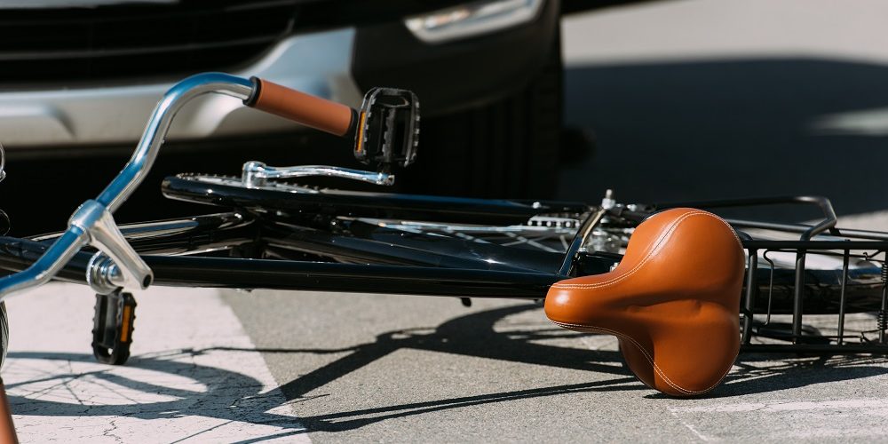 A bicycle is lying on its side on the street in front of a car, suggesting a recent accident—one of the common causes of bicycle collisions.