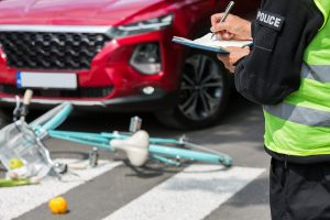  A cyclist wearing a helmet lies injured on a crosswalk after a hit-and-run bicycle accident, with a blue bicycle and personal items scattered nearby.