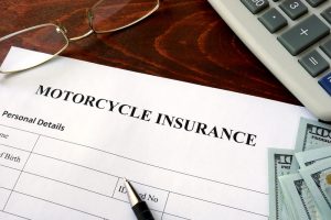 A motorcycle accident insurance form lies on a desk with a pen, eyeglasses, calculator, and several $100 bills.