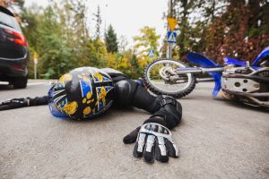 A person wearing a helmet and protective gear lies on the road next to a fallen motorcycle, indicating a recent motorcycle accident at an intersection.
