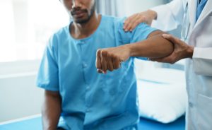 Doctor examining his patient arm in medical office while the patient sitting on hospital bed.