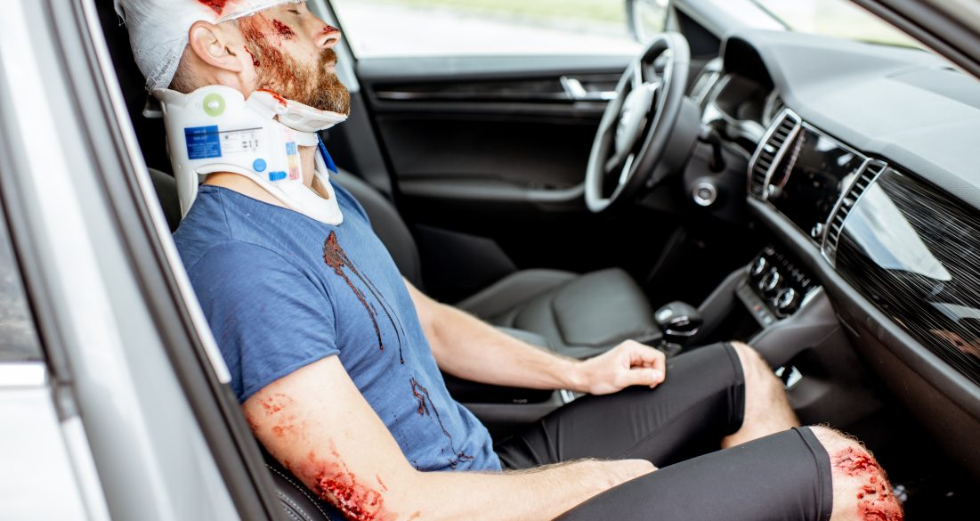 Injured man with deep wounds and corset on his neck sitting on the passenger seat during the medical assistance after the accident