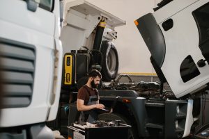 Auto mechanic using a laptop while examining a truck engine in a garage, conducting diagnostics and maintenance